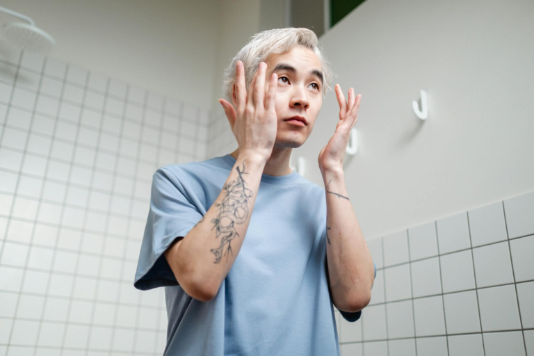Young man applying skincare product in a contemporary bathroom setting.
